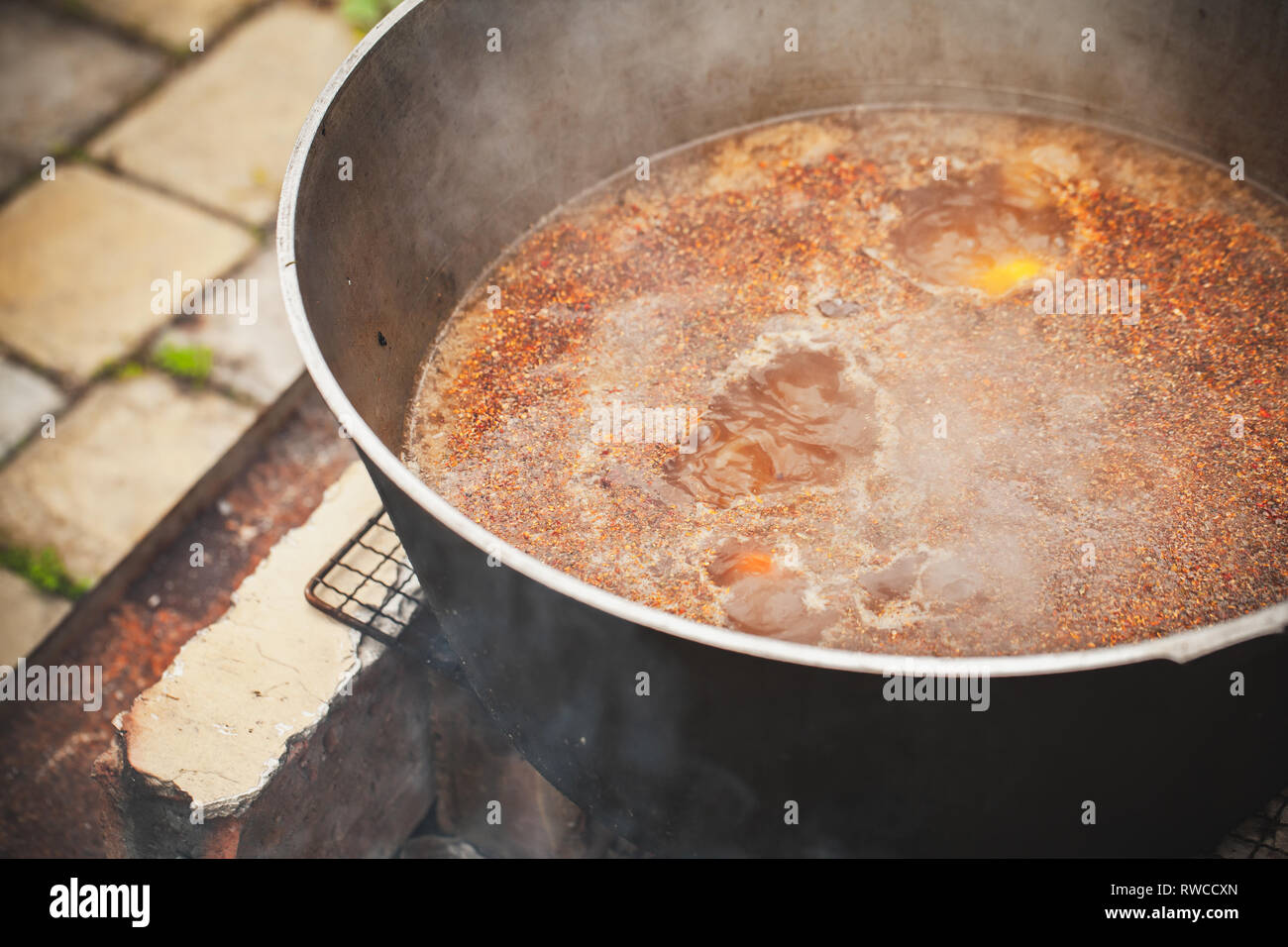 Spicy broth with lamb and vegetables boil in a cauldron. Preparing of Chorba soup on open fire, traditional meal for many national cuisines in Europe, Stock Photo