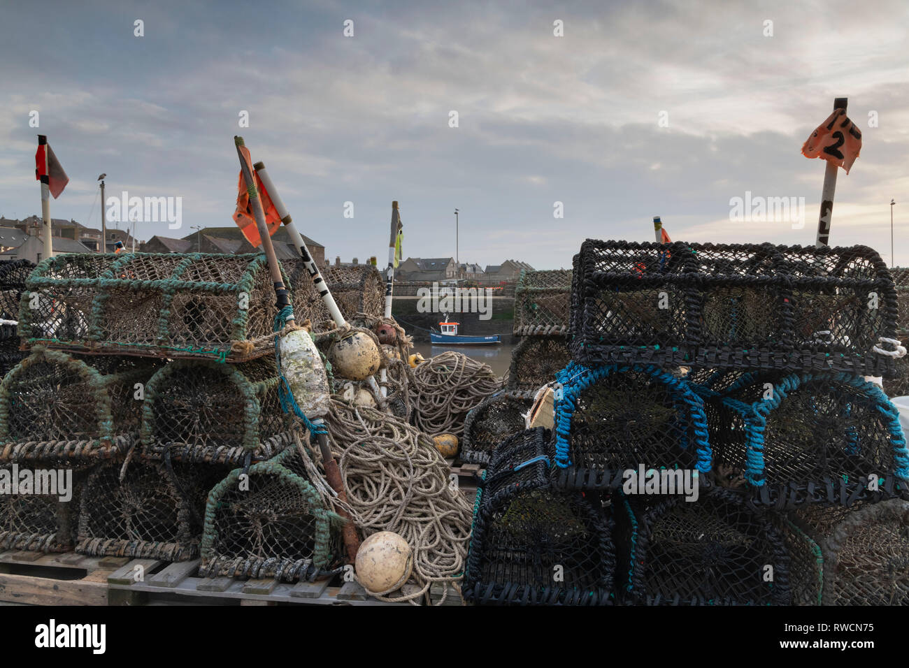 A Boat Moored Against the Wharf is Visible Through the Pile of Creels, Ropes and Marker Buoys on the Quayside at Gourdon Harbour Stock Photo