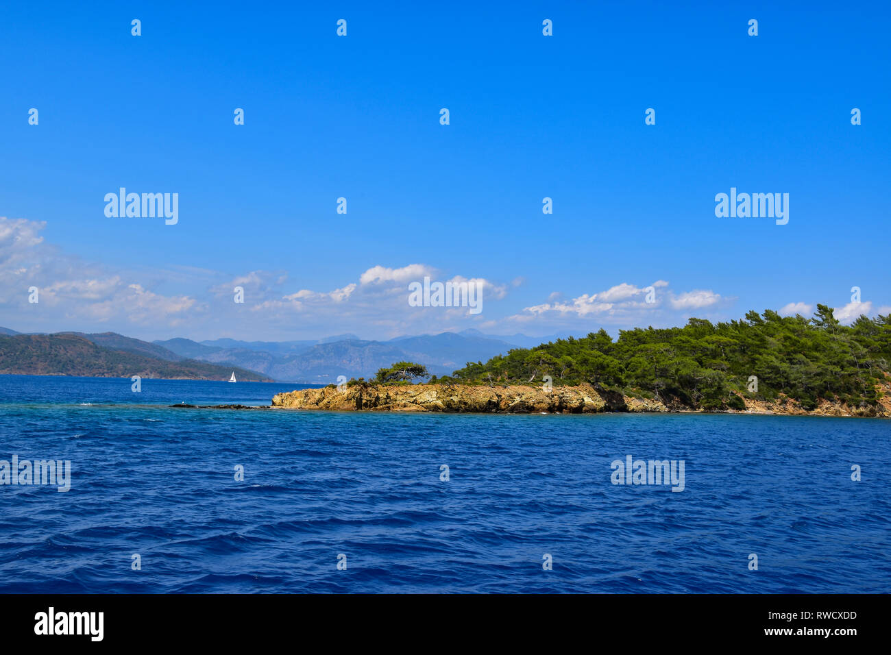 Distant sailing boat, pine trees, mountains and fluffy clouds, Gulet Boat Cruise, Mediterrean Sea, Turkey Stock Photo