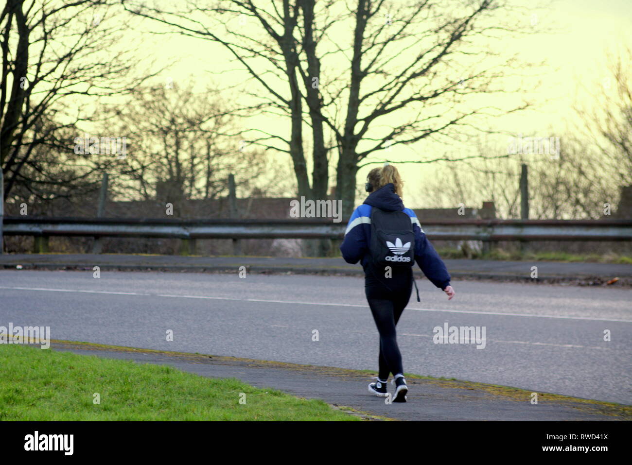 young girl student schoolgirl with adidas rucksack, bag walking alone on street drumchapel, Glasgow, Scotland, UK, Stock Photo
