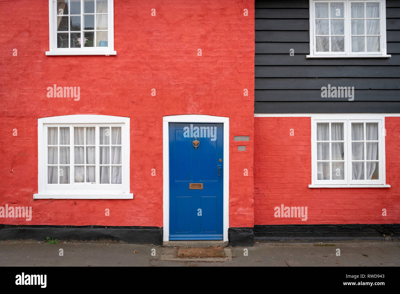 A brightly coloured cottage in a UK village with red walls and a blue door. Stock Photo