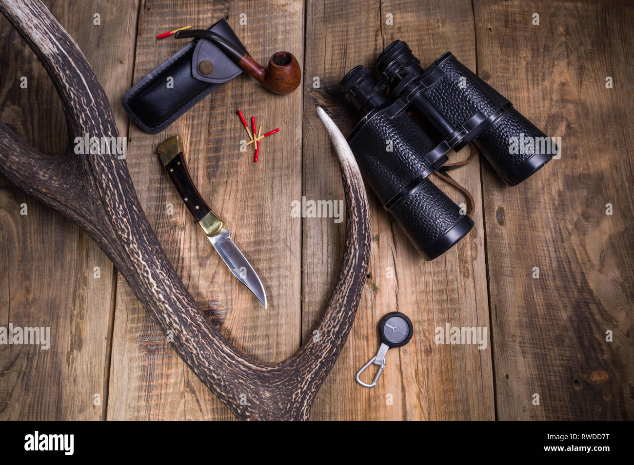 A hunting knife, binoculars and a cradle for tobacco. Deer horn and tree in the background. Top. Stock Photo
