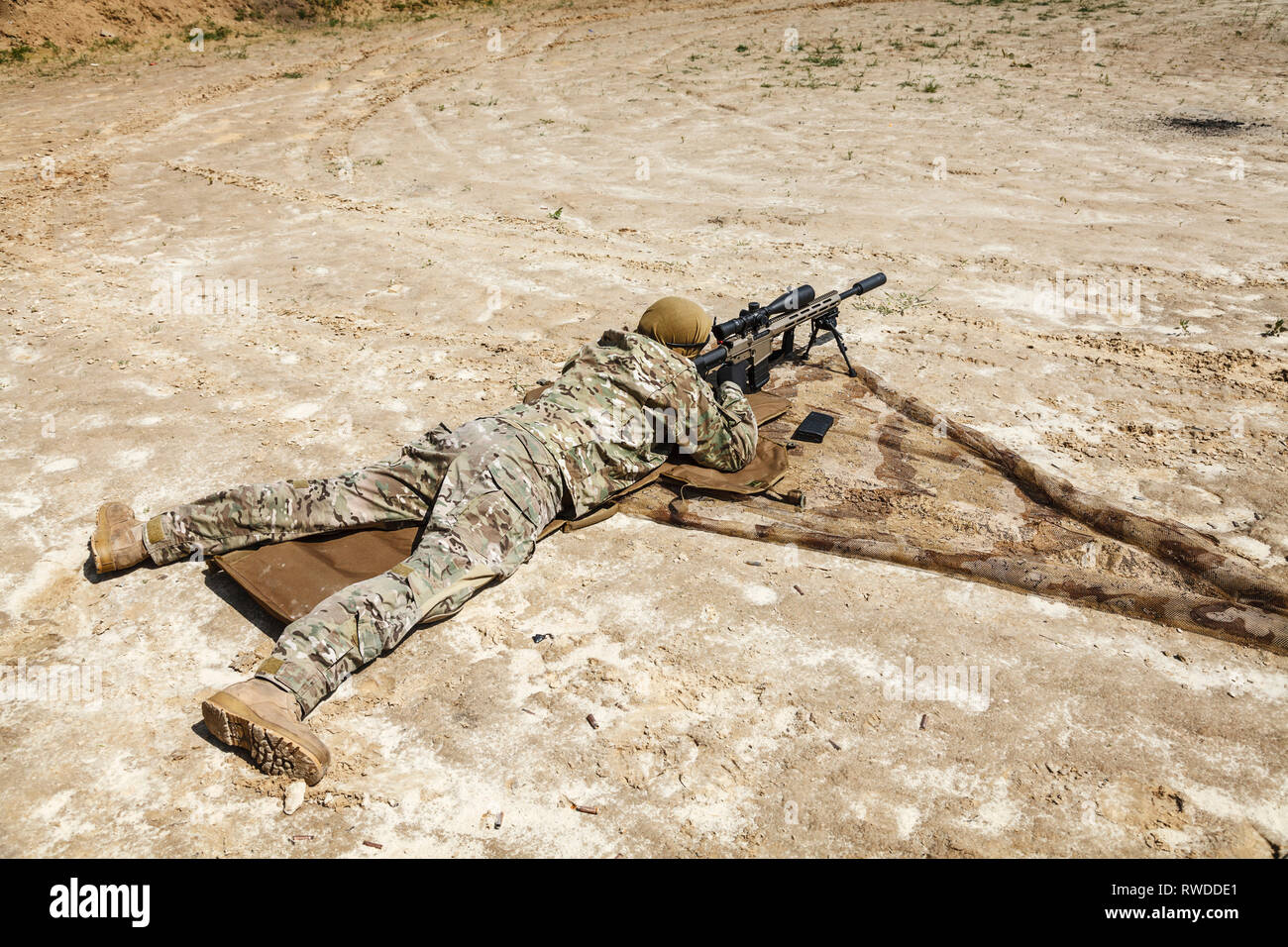 Young male sniper in camouflage with gun in the desert. Stock Photo