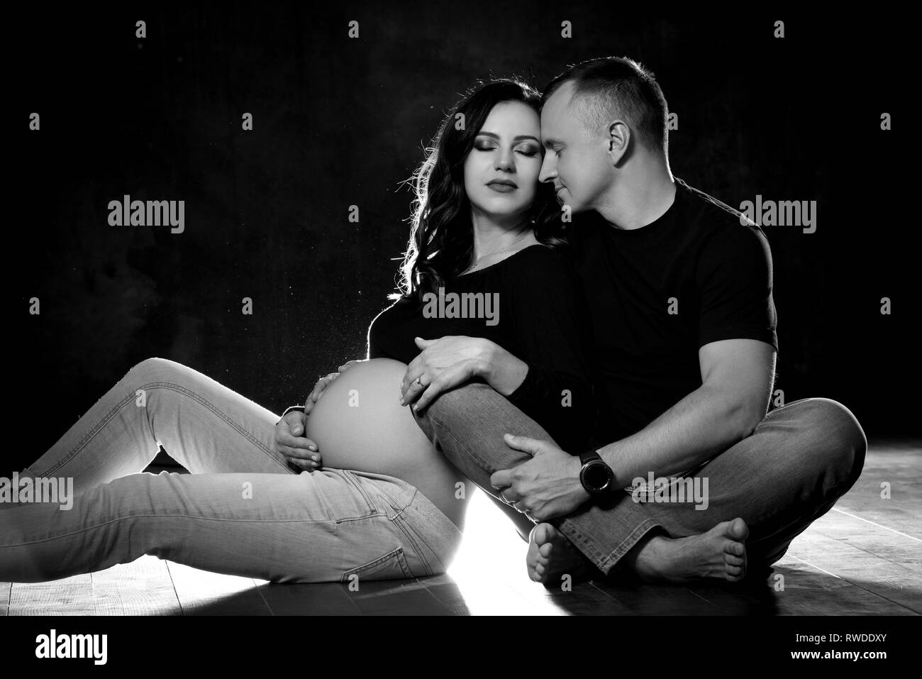 Handsome pregnant couple woman and man an posing on dark black ...