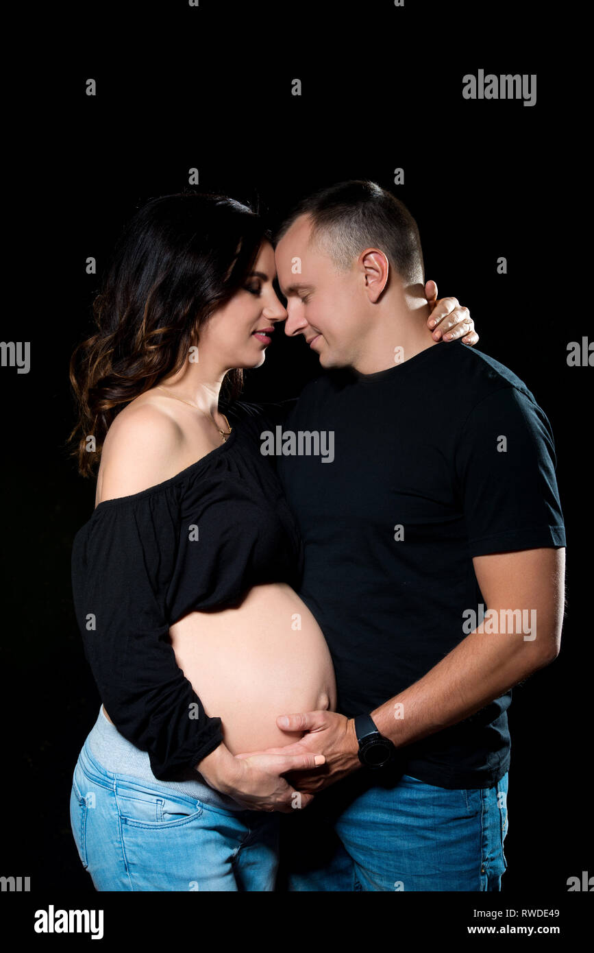 Handsome pregnant couple woman and man posing on dark black background ...