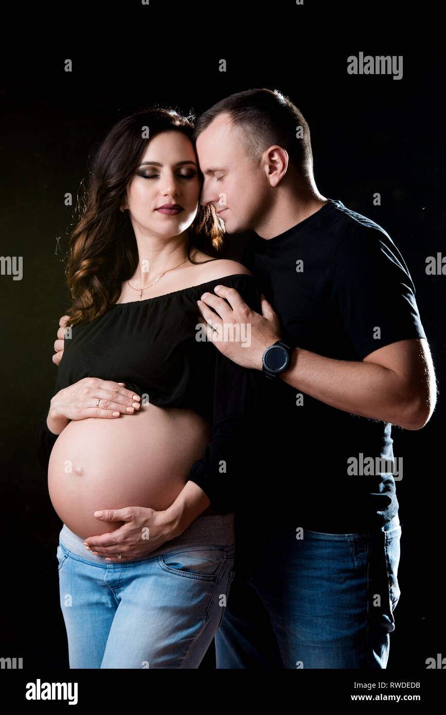 Handsome pregnant couple woman and man an posing on dark black ...