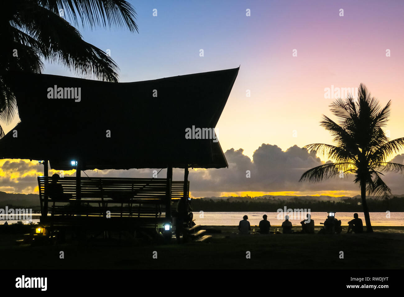 Surfer friends Sitting at beach Bungalow - Cloud 9 Sunset - Siargao, Philippines Stock Photo