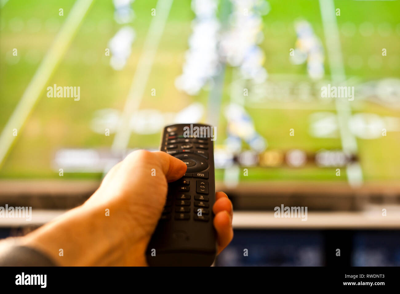 hand holding a remote control in front of the tv screen Stock Photo