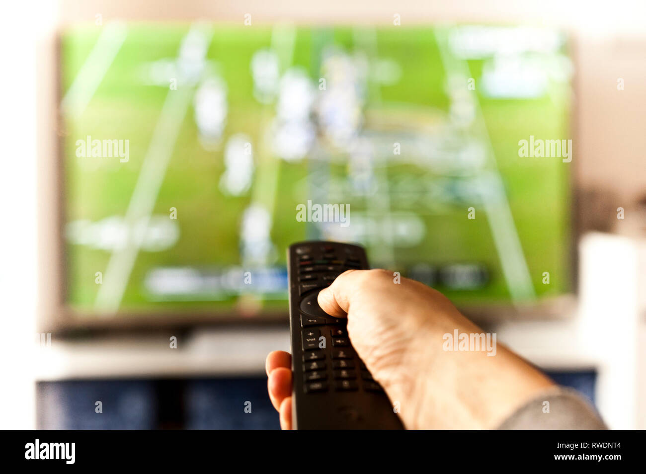 hand holding a remote control in front of the tv screen Stock Photo
