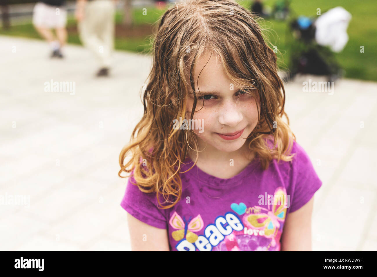 A ten-year-old girl with curly blond wet hair looks unhappy about having her photo taken in a park in Boston, Massachusetts. Stock Photo