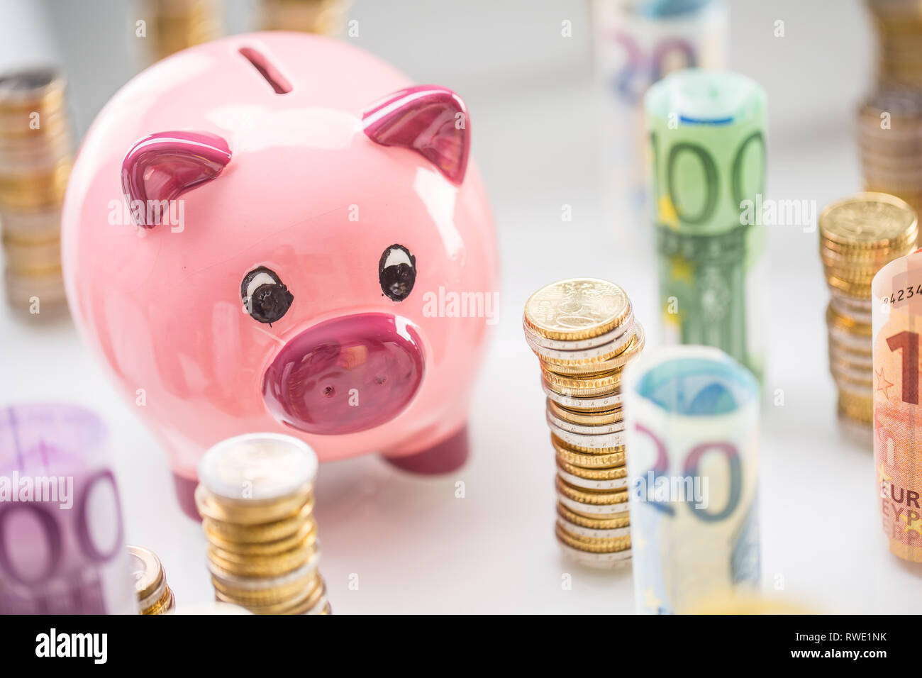 Pink piggy bank in the middle of rolled euro banknotes and towers with ...