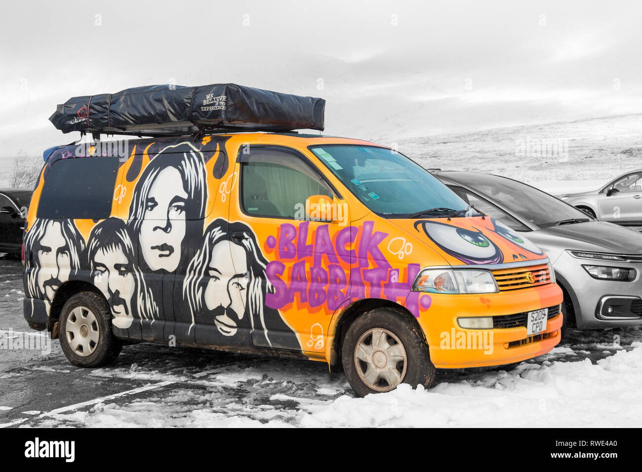 Wicked Campers Black Sabbath painted campervan parked in snow covered car park at Glencoe mountain resort at Glencoe, Highlands, Scotland in Winter Stock Photo