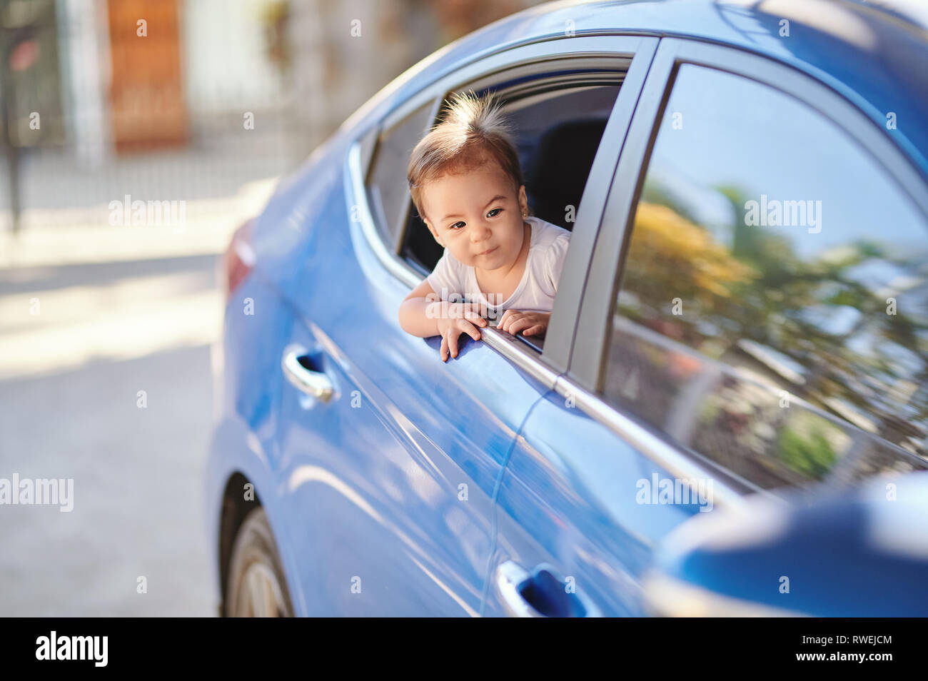 Excited baby girl looking out from car window on sunny day Stock Photo