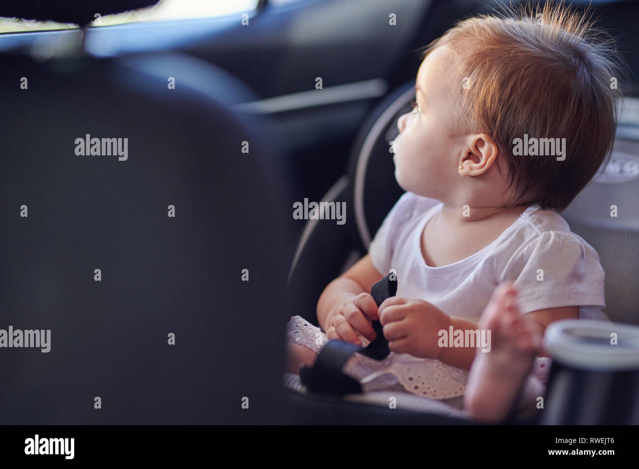 Baby girl look at car window. Small girl travel in car seat Stock Photo