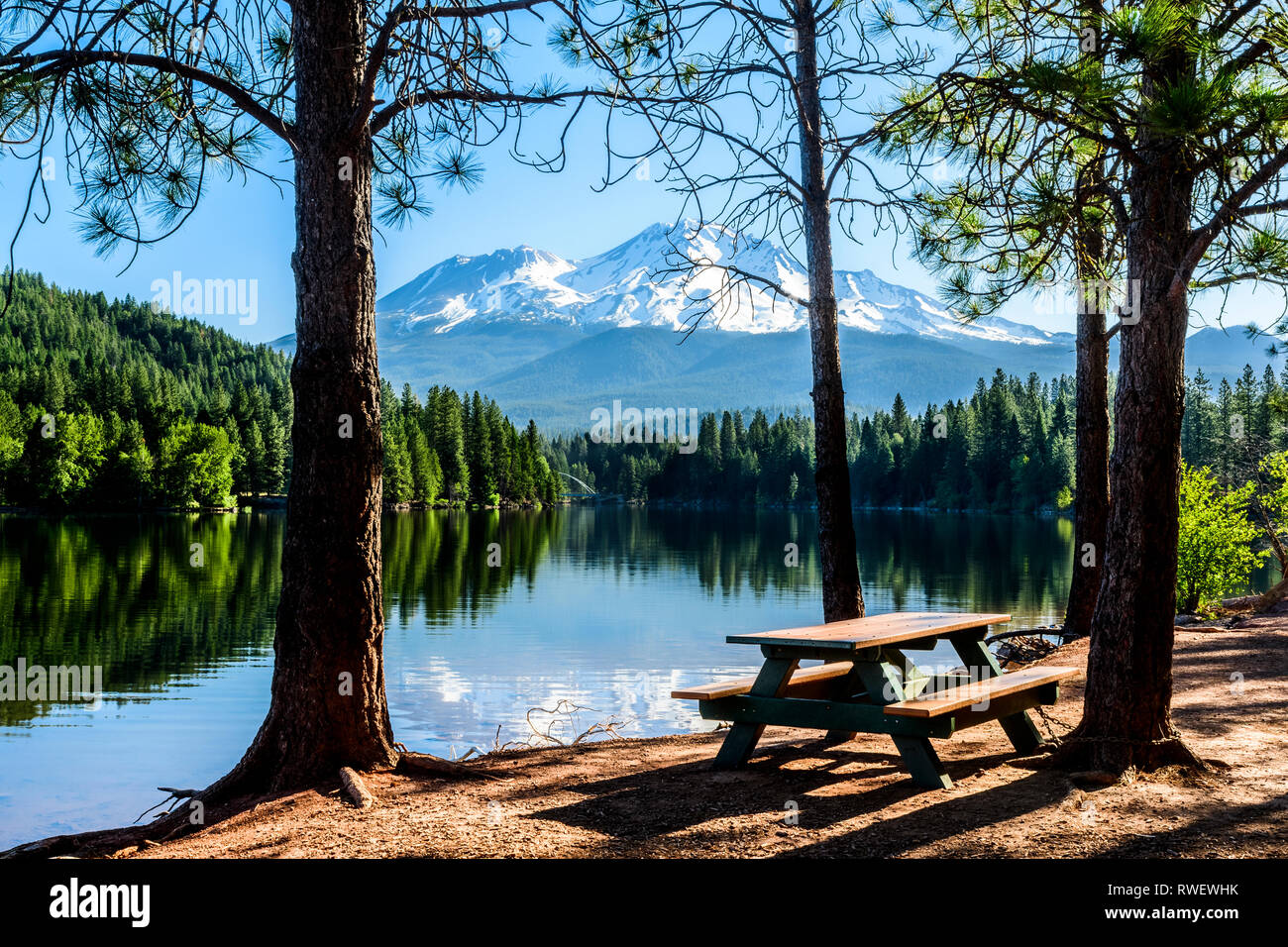 A picnic table at the edge of Siskiyou Lake in Lake Siskiyou Park near Mt. Shasta, California, USA.  Mt. Shasta is in the background. Stock Photo