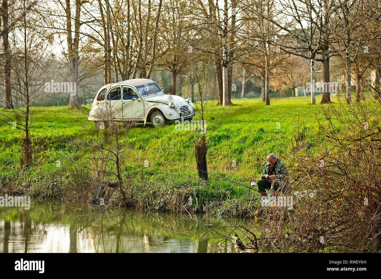 Citroen 2CV and fisherman beside Dropt River near Eymet, Dordogne Department, Aquitaine, France Stock Photo