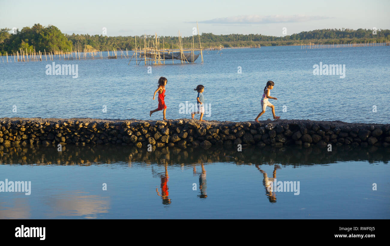 Young girls running along a lagoon by the sea - Donsol, Sorsogon, Philippines Stock Photo
