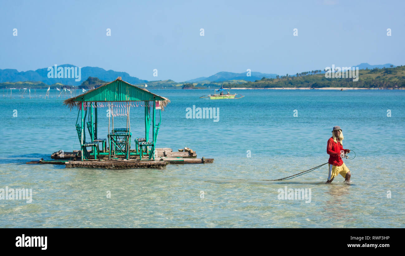 Man dragging floating hut through water - Manlawi Sandbar, Caramoan, Philippines Stock Photo