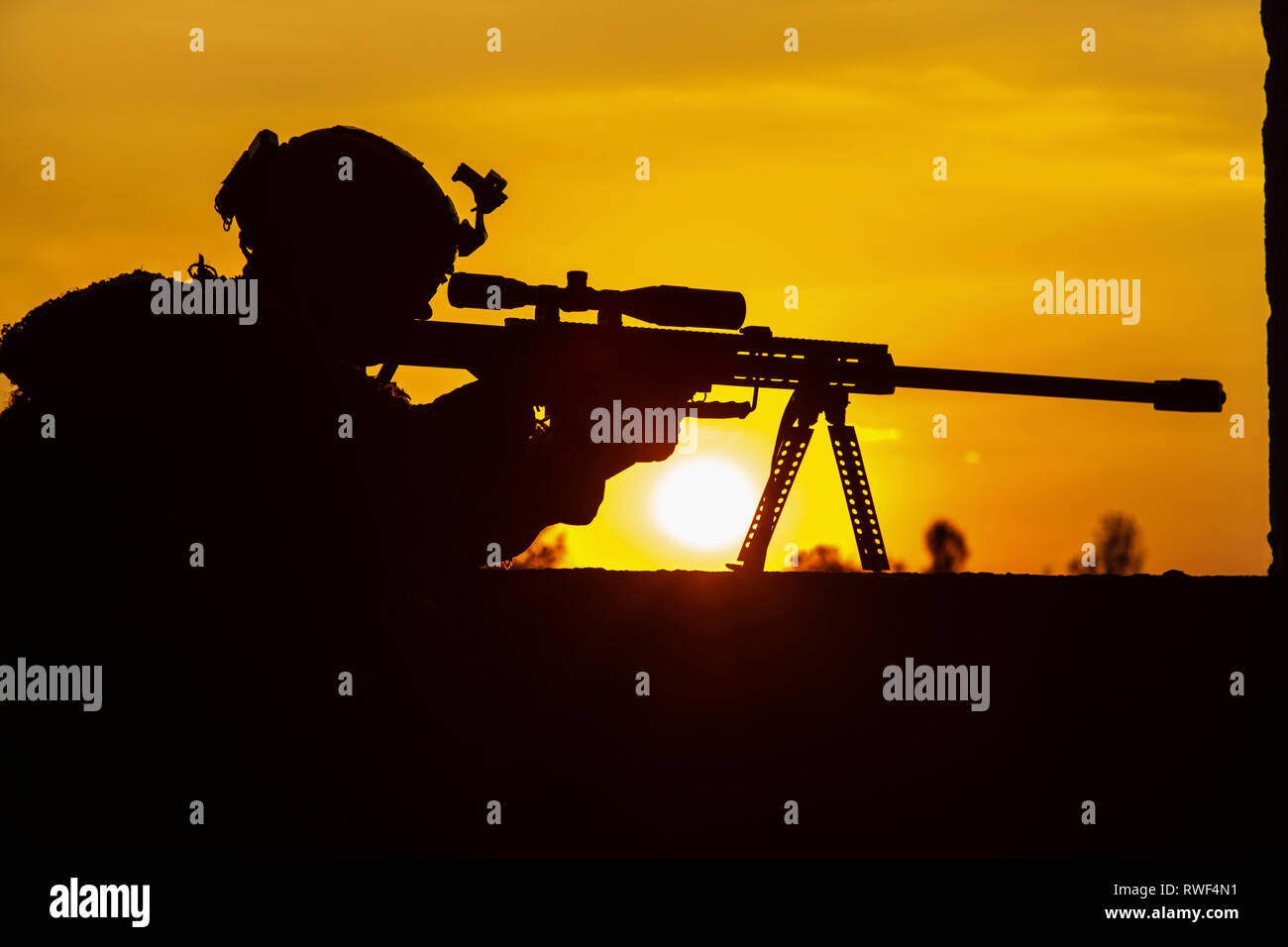 Silhouette of Army sniper with large-caliber rifle against sunset. Stock Photo
