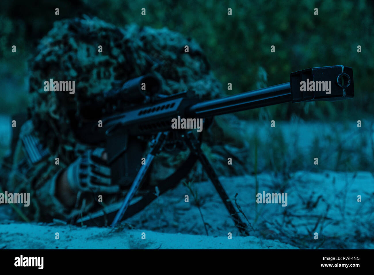 Army sniper with big rifle lying in the forest at night. Stock Photo