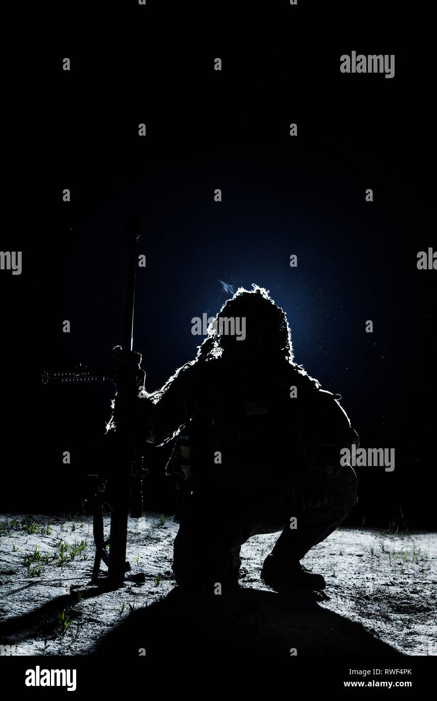 Army sniper sitting, holding rifle, on black background. Stock Photo