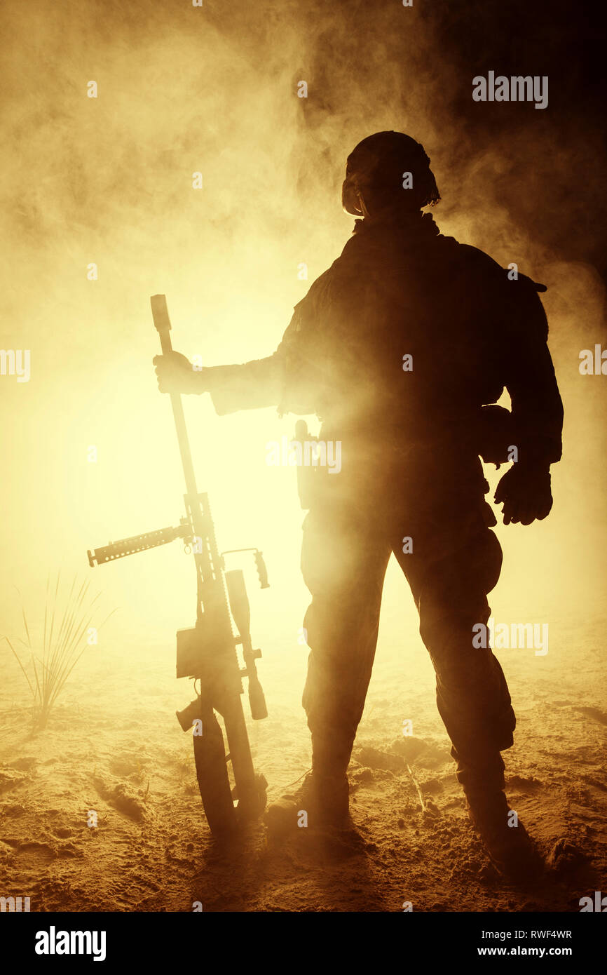 Backlit silhouette of Army sniper with large caliber rifle standing in ...