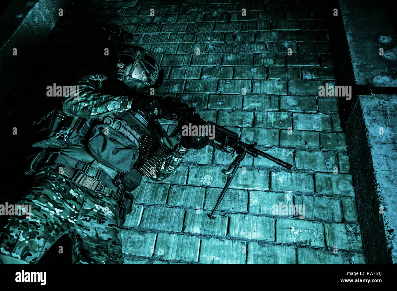 U.S. Army Ranger with machine gun and night vision goggles moving along the wall during a mission. Stock Photo