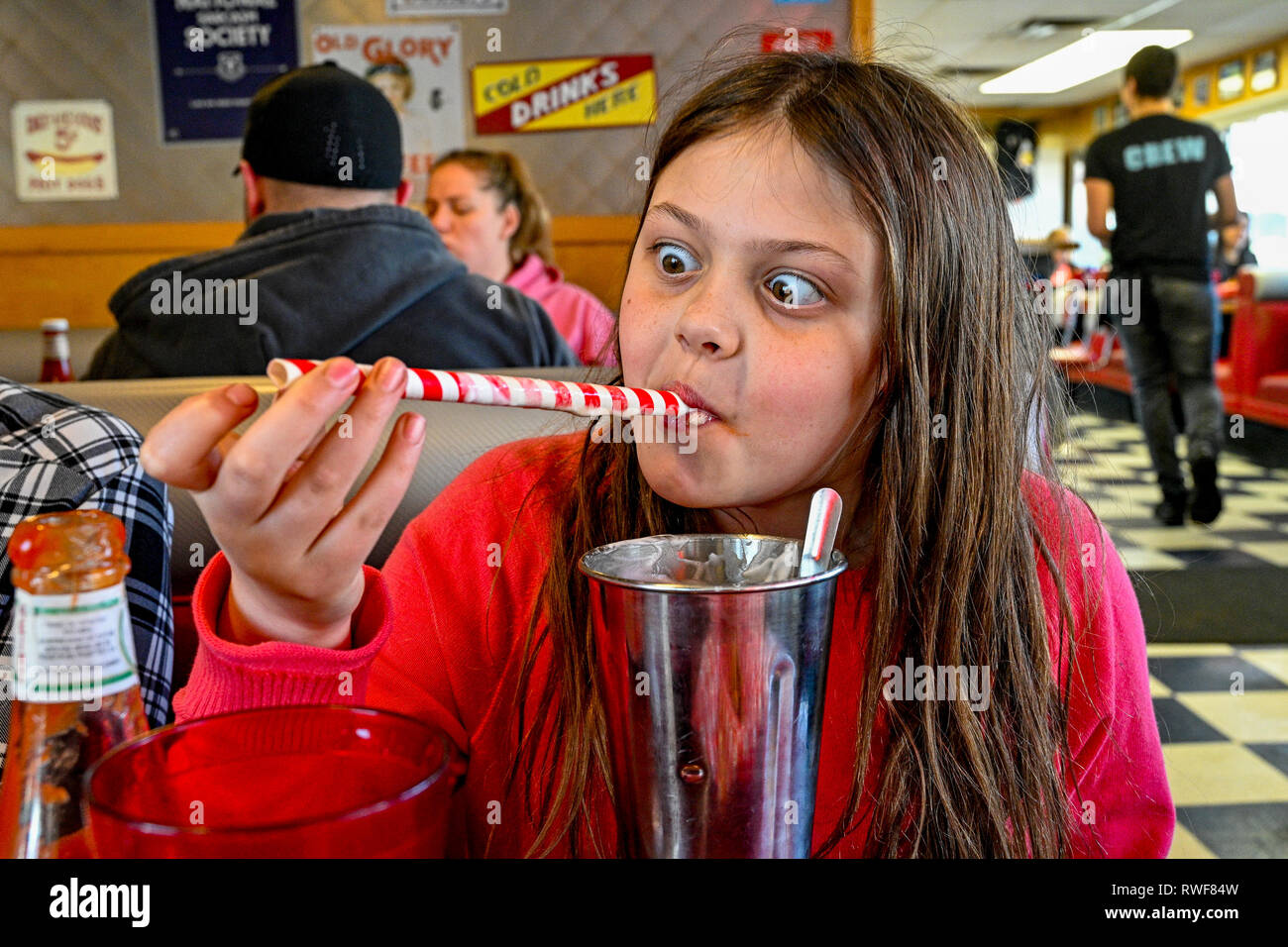 Young girl deliberately crossing her eyes while using milkshake straw  at fast food restaurant Stock Photo