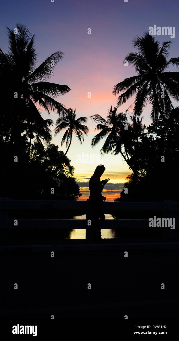 Island Girl Checking Her Phone, With Palm Tree Silhouettes During Sunset - Boracay Island - Philippines Stock Photo