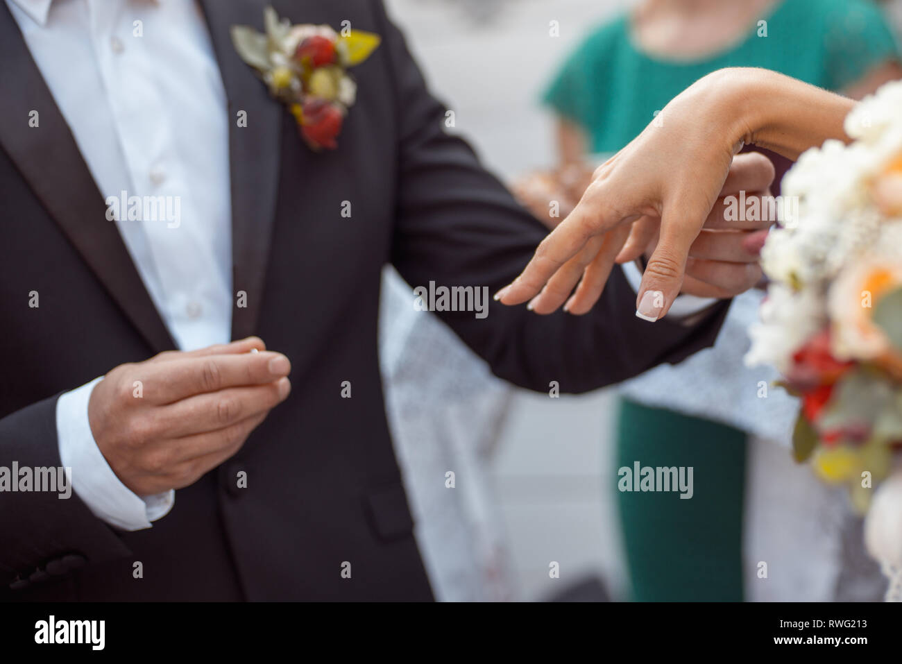 Groom In a dark blue jacket with a boutonniere puts a ring on the bride's hand. close-up shot of chest cropping Stock Photo