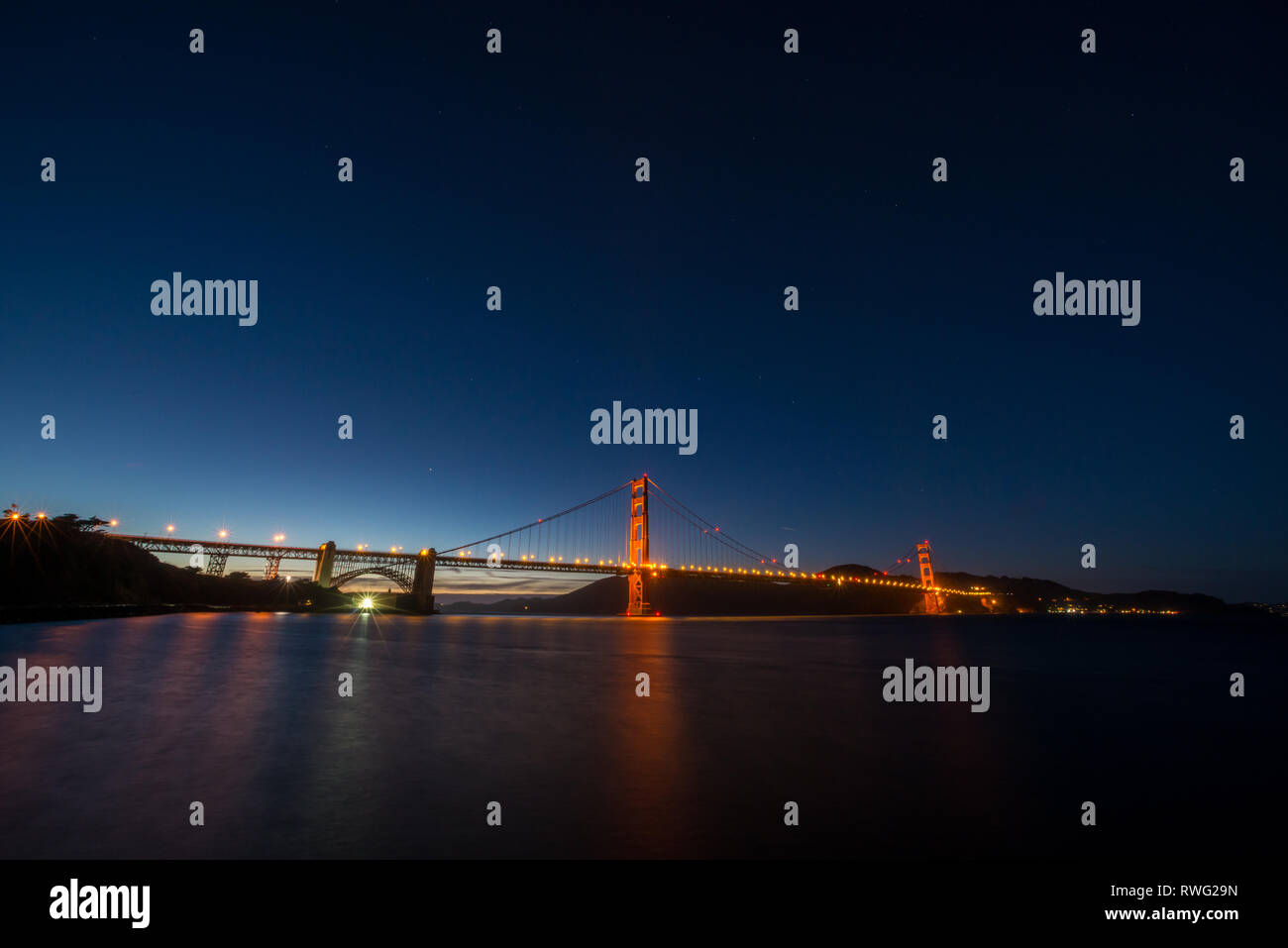 Golden Gate Bridge illuminated by streetlights rises above the water after sunset Stock Photo