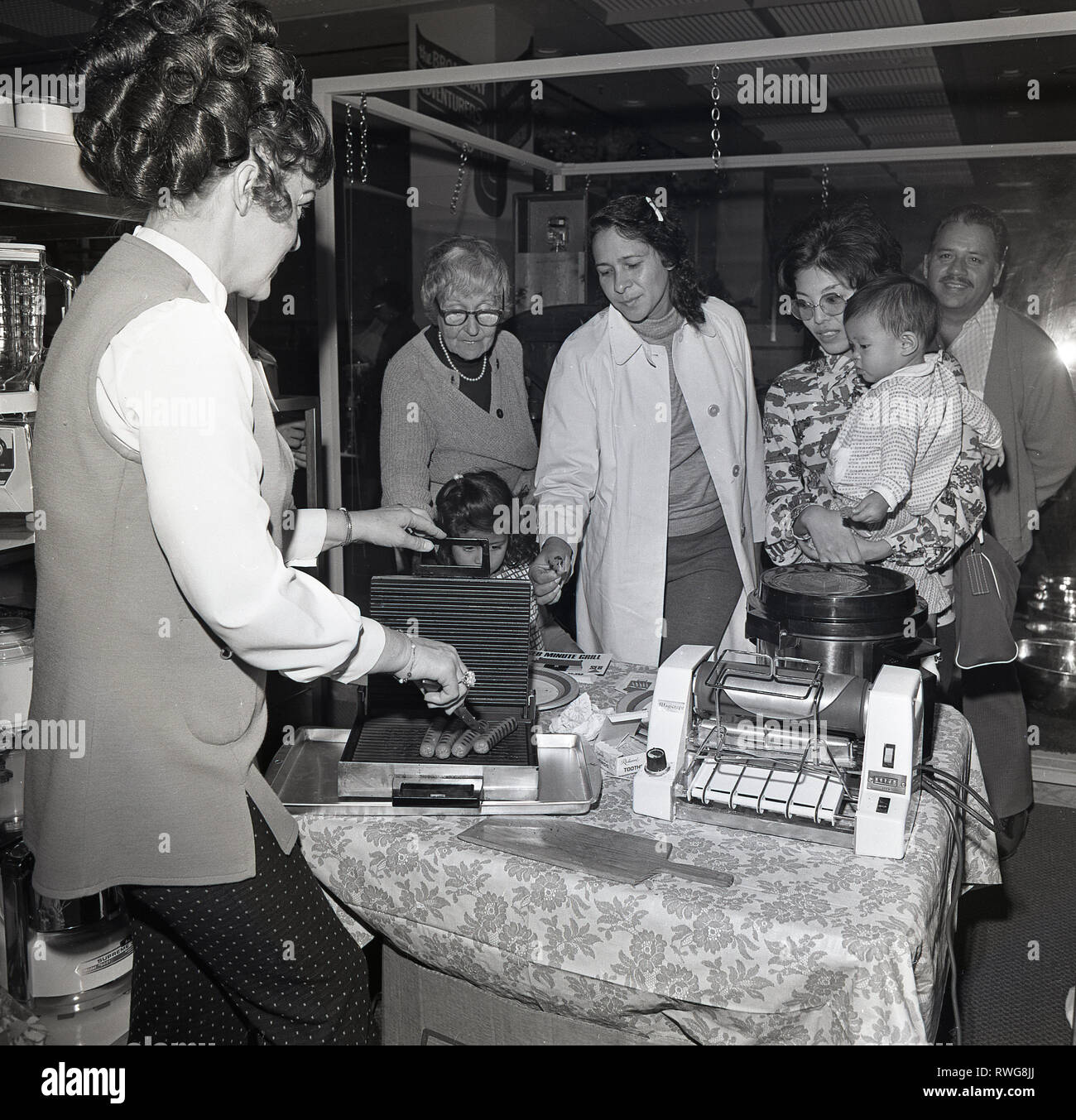 1970s, in-store, kitchen appliance demo, a lady demonstrating to potential customers how to cook food, 'hotdogs' quickly on a new 'minute grill', Los Angles, USA. Stock Photo