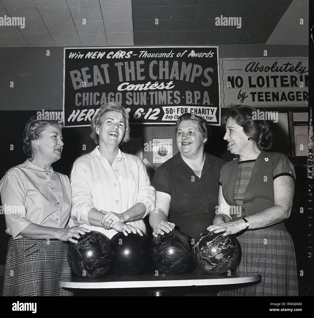 1950s, lady players at a bowling alley standing with their bowls having a laugh together, Chicago, USA. A sign behind them says Win New Cars, Beat The Champs Contest promoted by the Chicago Sun Times. Also beside this, another sign saying.... 'Absolutely No Loitering by Teenagers'. Stock Photo