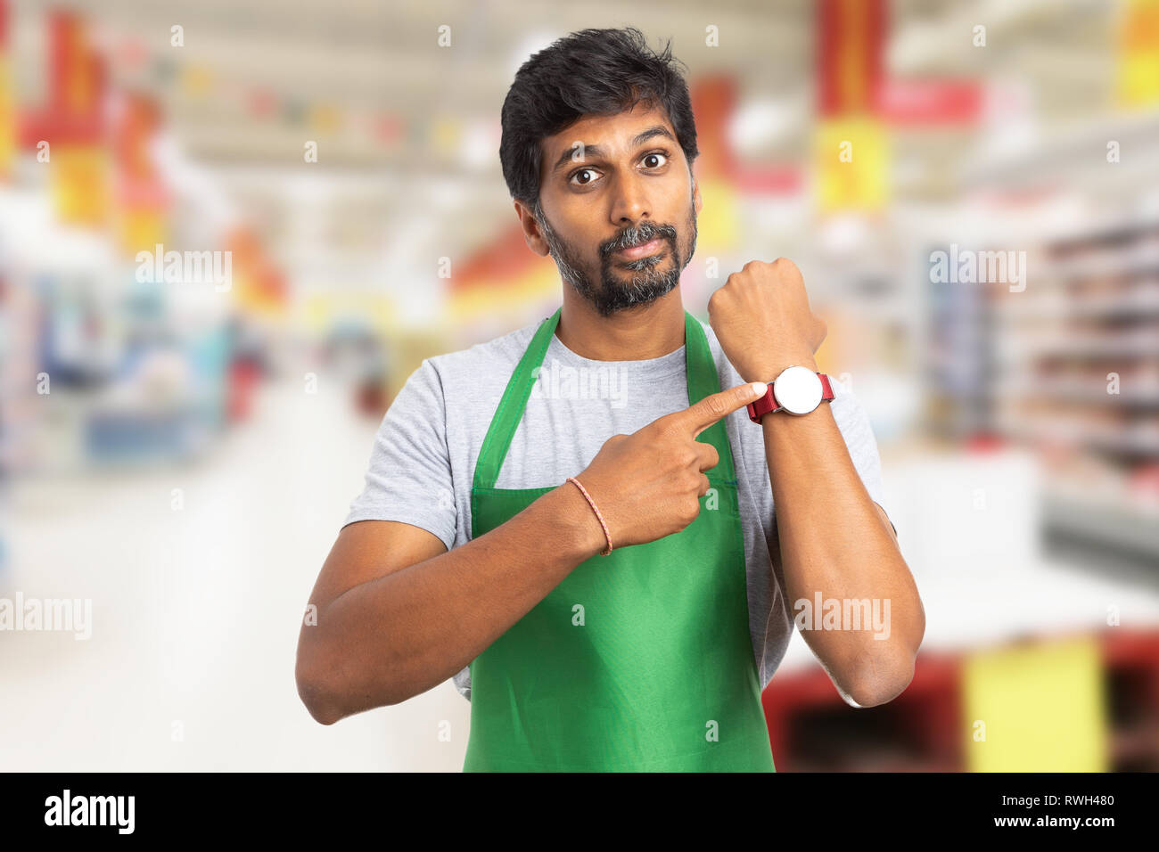 Indian manager man at hypermarket or supermarket showing wristwatch with index finger and angry expression as you are late concept Stock Photo
