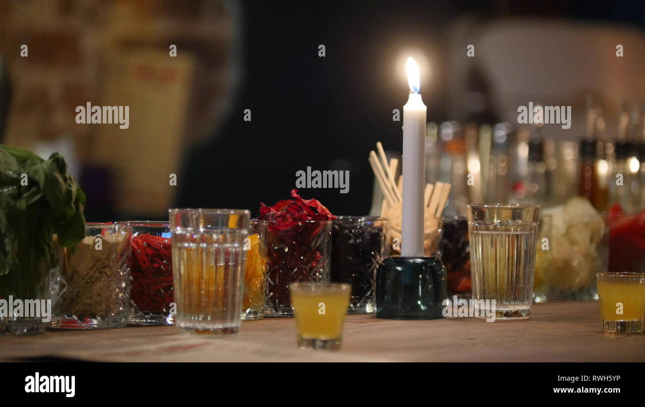 Colored cocktail ingridients in glasses and a candle stand on a bar