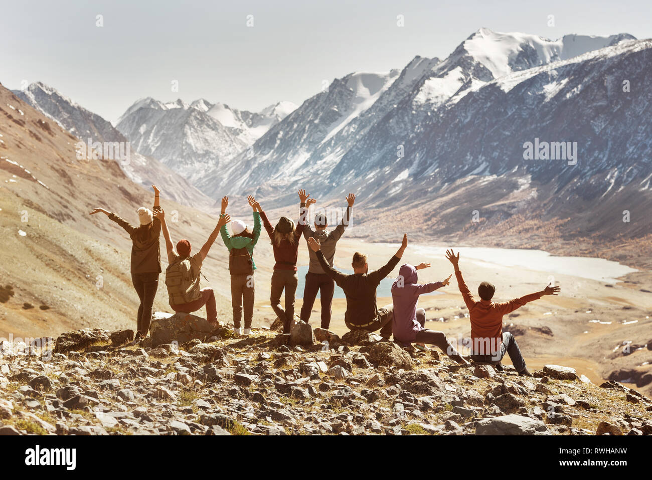 Big happy active company of friends sits in mountains and having fun with raised arms Stock Photo