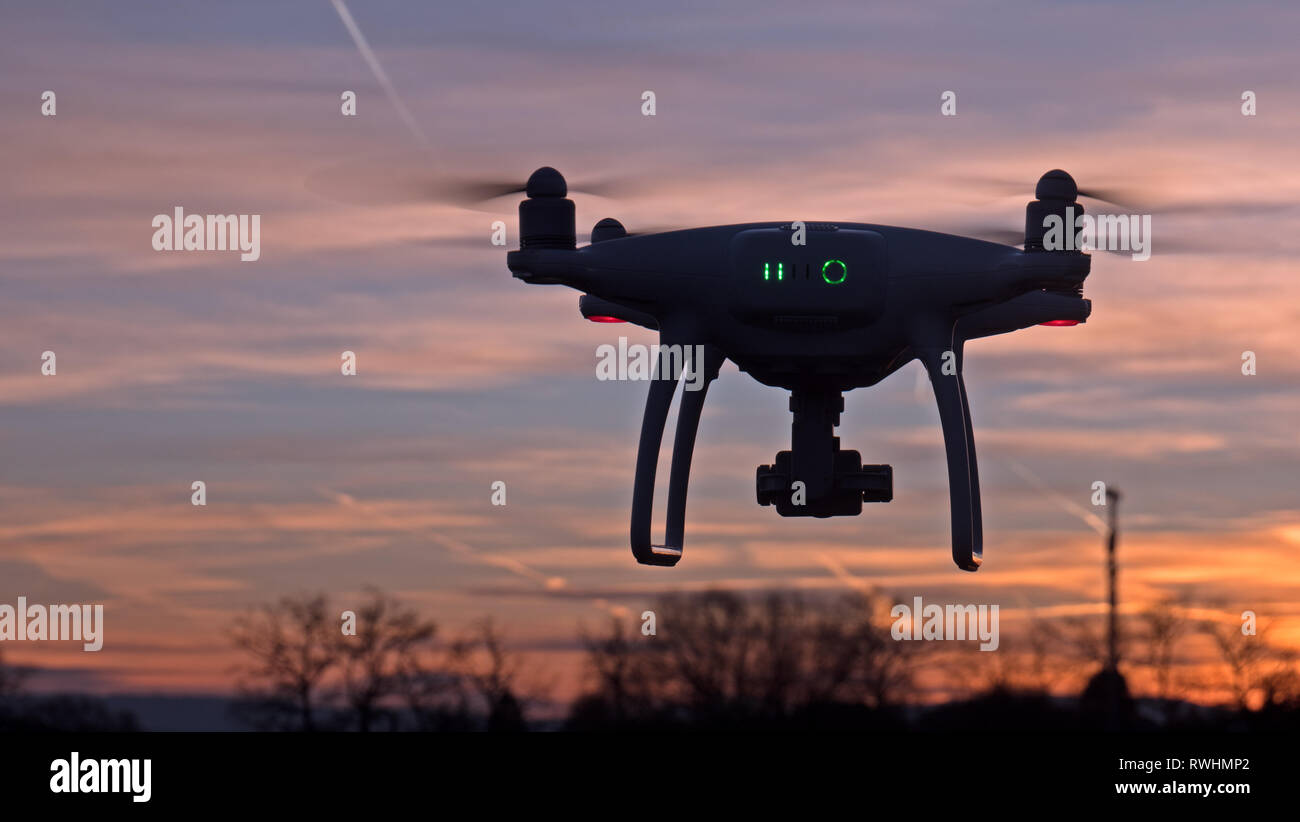 A drone hovers in flight in front of a sunset background. The drone is stationary hovering above the ground as the sunsets in the distance. Stock Photo