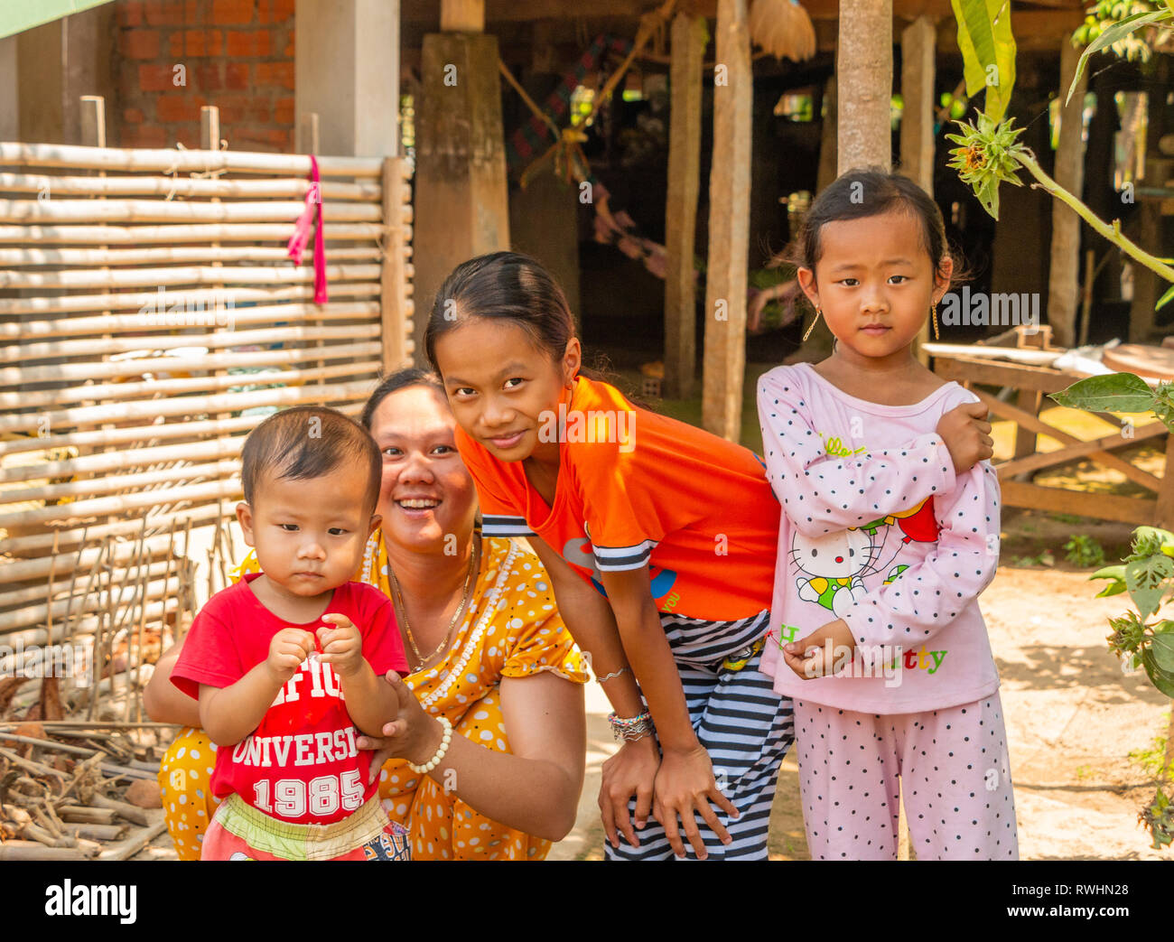 3 young happy, smiling Vietnamese  children of mixed ages wearing pyjamas with their mother outside their home  Tan Chau, Mekong Delta, Vietnam Stock Photo