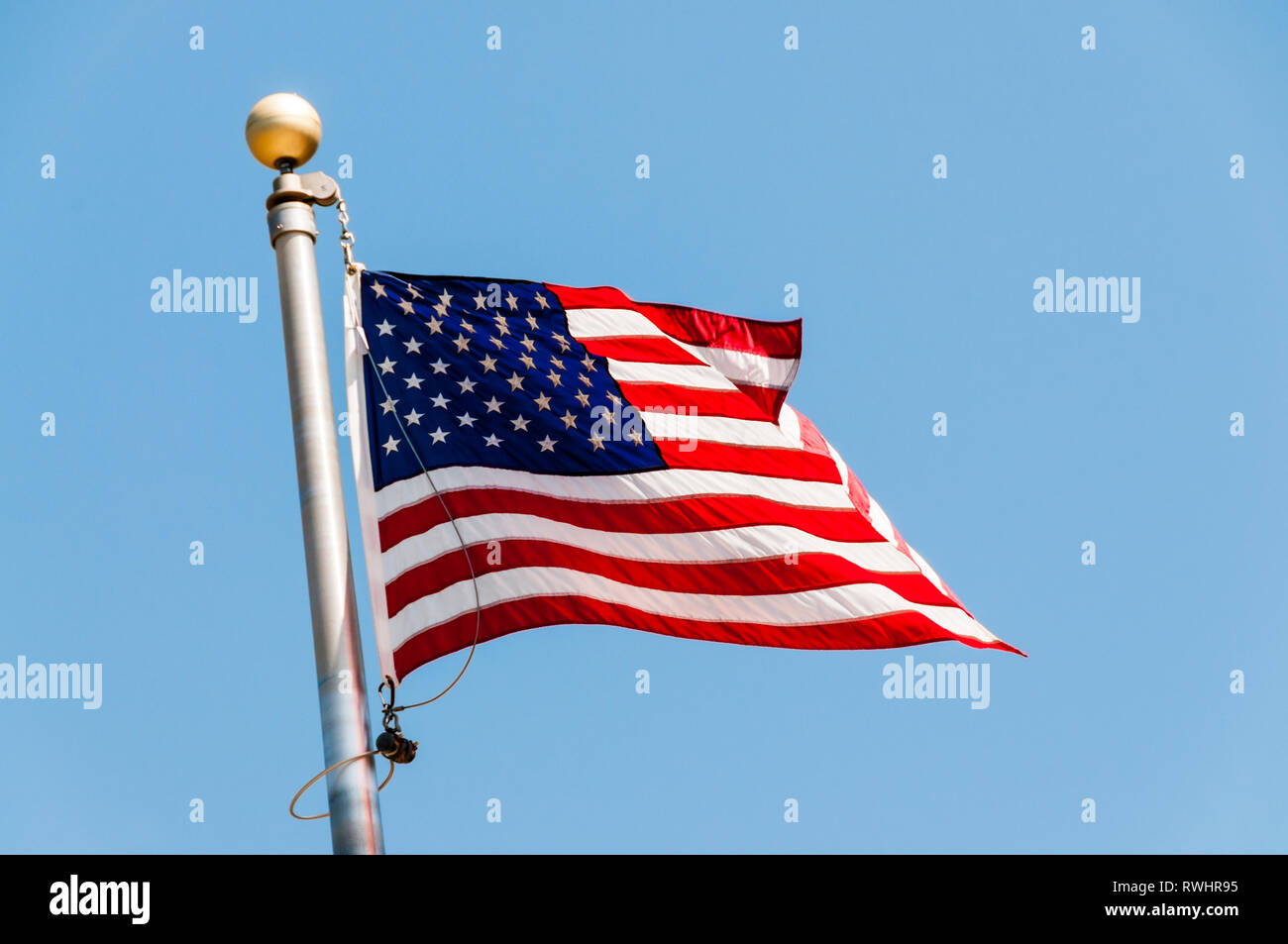 The American flag or stars and stripes flying against a blue sky. Stock Photo