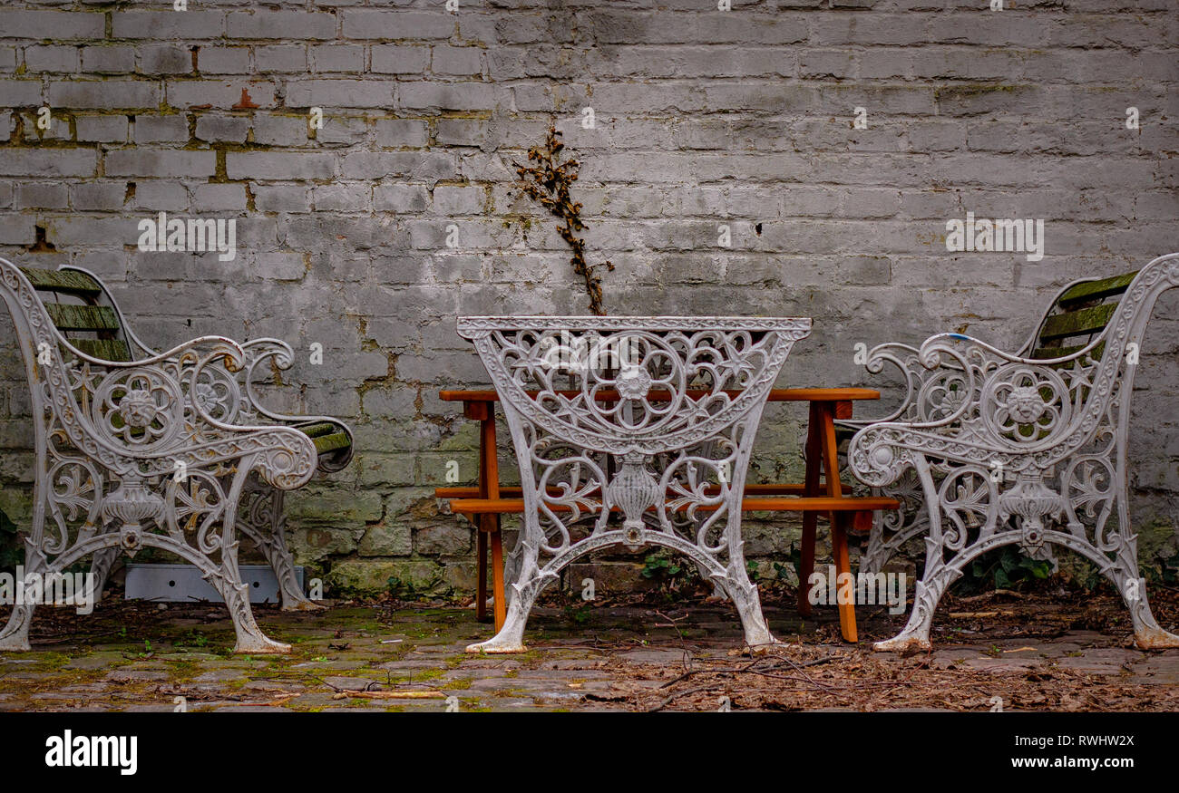 Two iron vintage benches and a table front of a wall Stock Photo