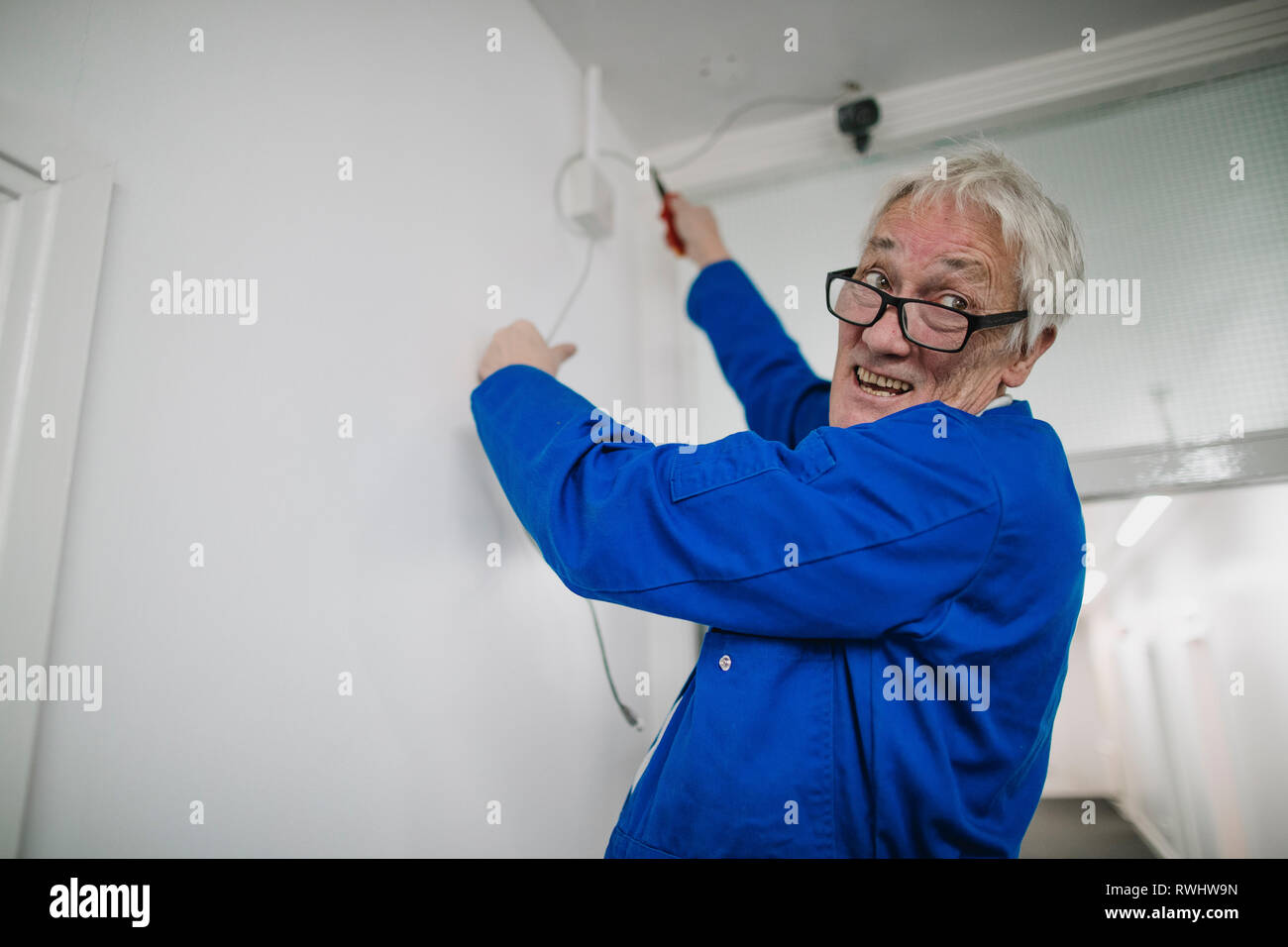 Senior electrician is fitting a security camera system in an office corridor. Stock Photo
