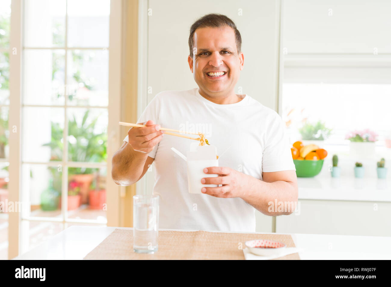 Middle age man eating take away noodles with choopsticks at home Stock Photo