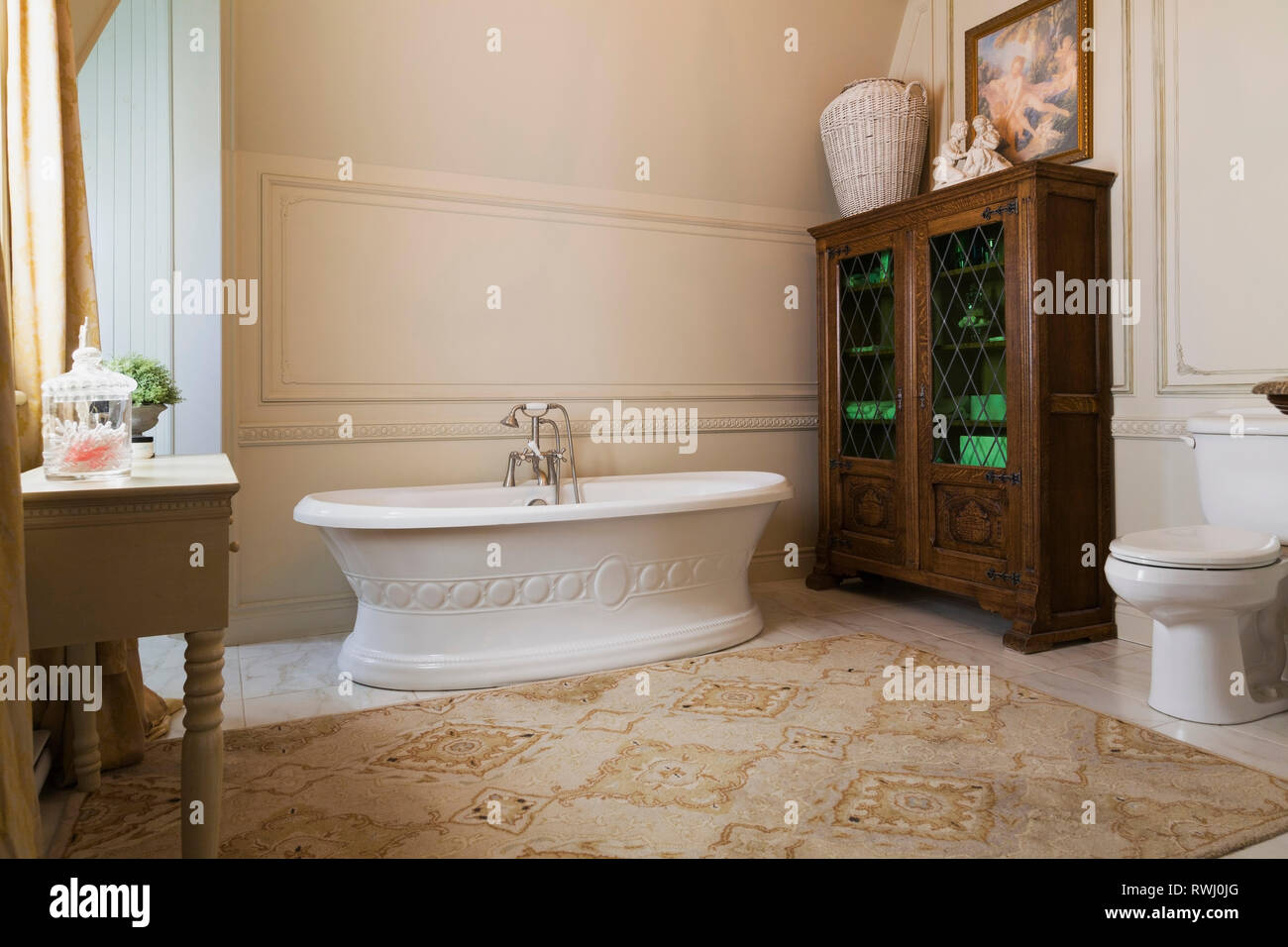 Freestanding boat style bathtub and wooden cabinet with leaded glass panels in the master bathroom on the upstairs floor inside a 2006 reproduction of a 16th century Renaissance castle style residential home, Quebec, Canada Stock Photo