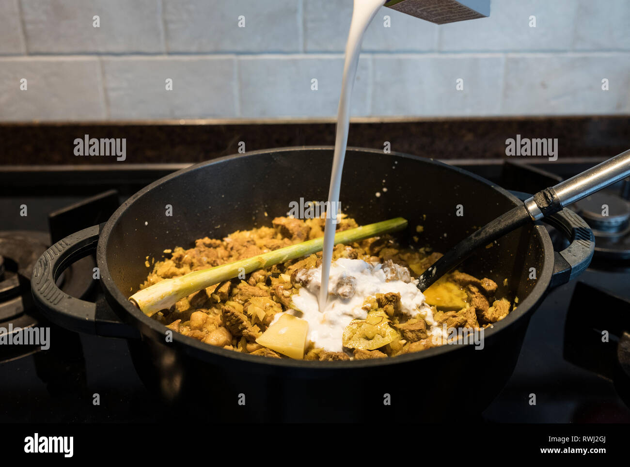 adding the coconut milk in a pan on the gas stove with indonesian rendang, a stew with beef Stock Photo