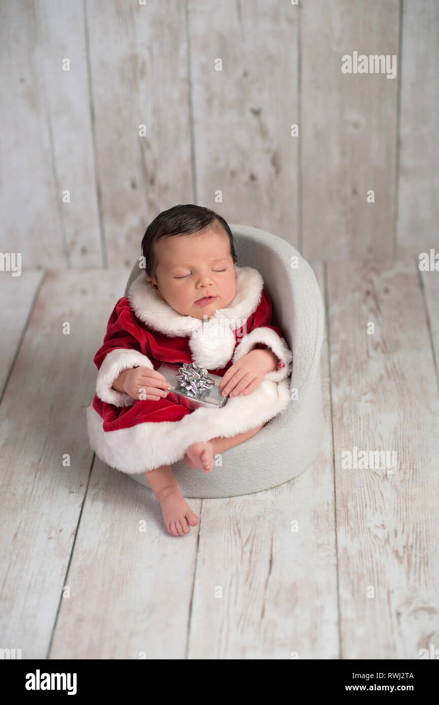 Portrait of one week old newborn baby girl sleeping in a chair and wearing a red and white Mrs. Claus dress. Stock Photo