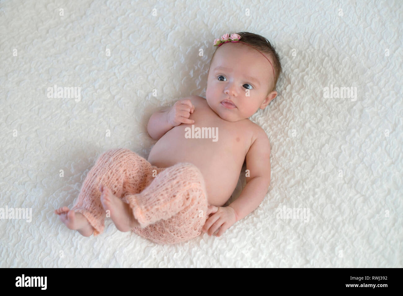 Portrait of an alert, one month old, baby girl wearing knitted, pale pink pants. Stock Photo