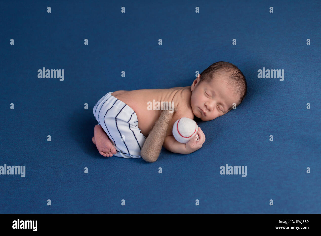 A week old, sleeping, newborn baby boy wearing baseball uniform pants and holding a baseball. Stock Photo