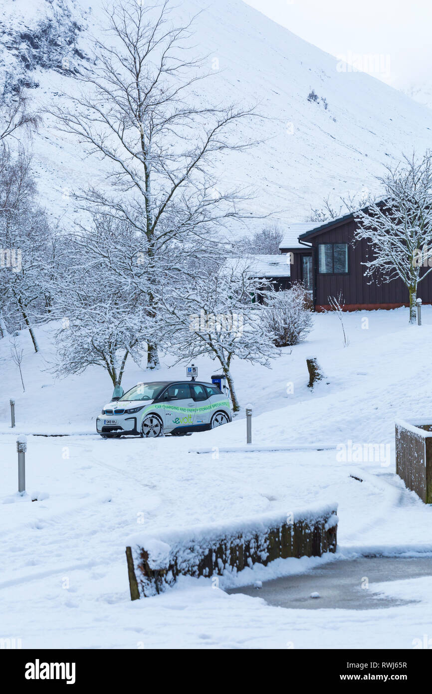 BMW Electric car being charged at electric car charging station point in snow covered car park by Clachaig Inn, Glencoe, Highlands, Scotland in Winter Stock Photo