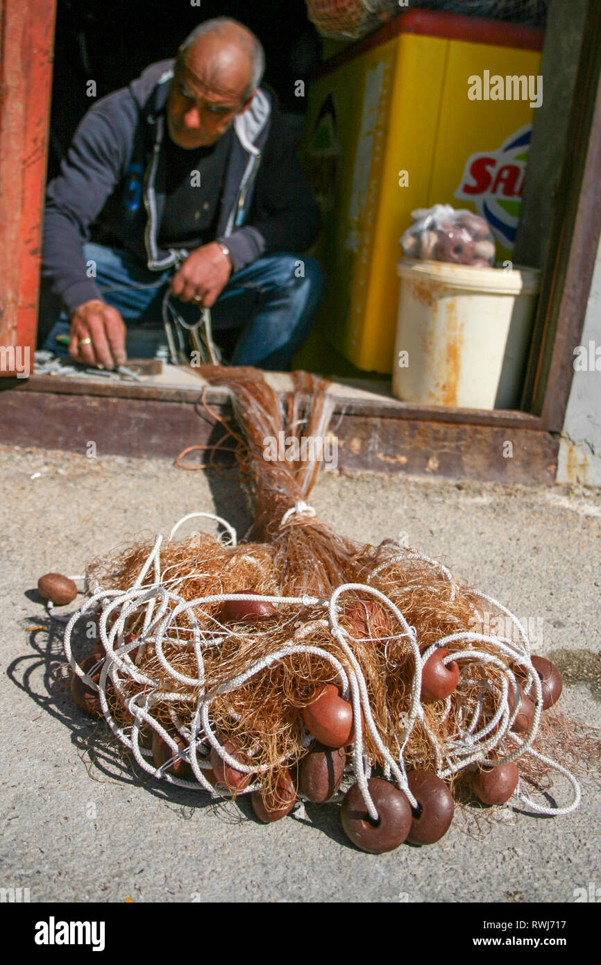 Fisherman repairing fishing net with cords and floats Stock Photo