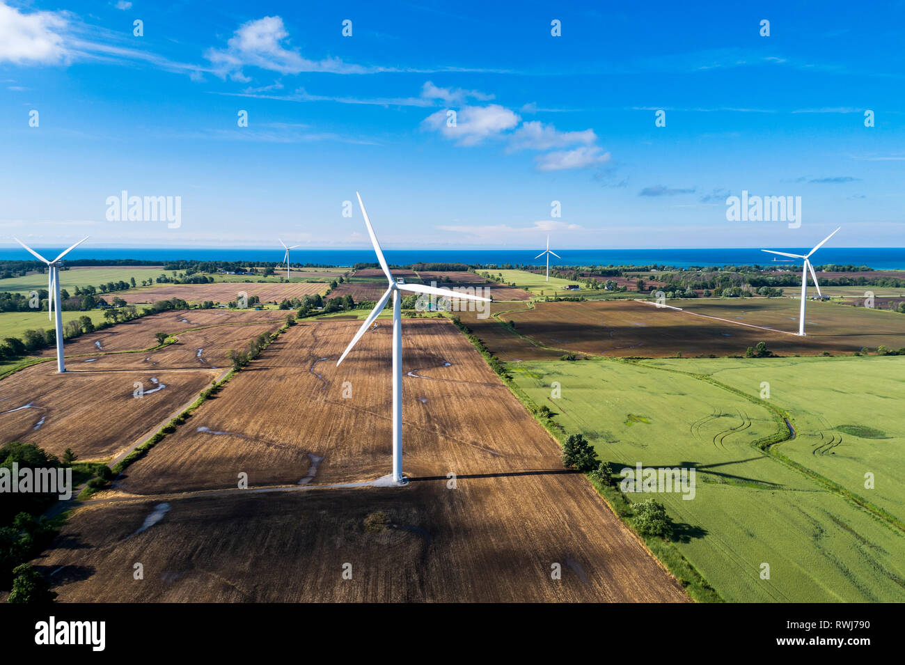 Large wind turbines on farm fields with a lake in the background and blue sky with clouds, West